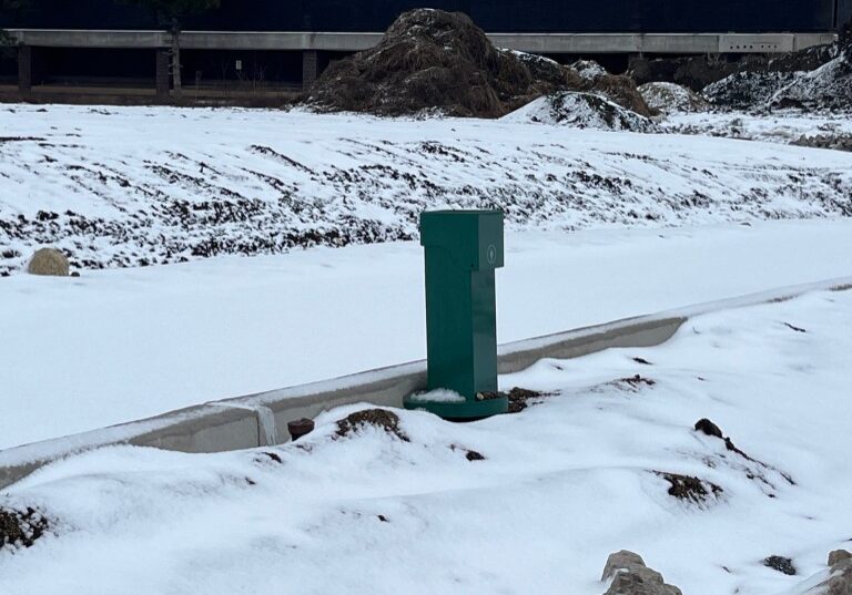 A Pedoc power pedestals installed near a sidewalk in snowy conditions at a corporate campus.