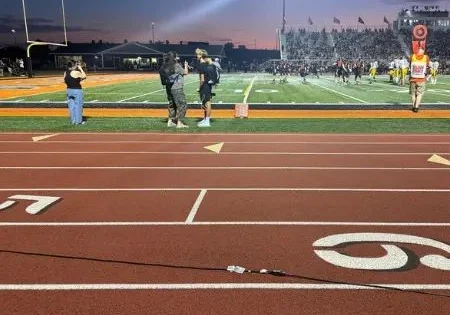 Power cord running across a stadium track during an outdoor football game at night.