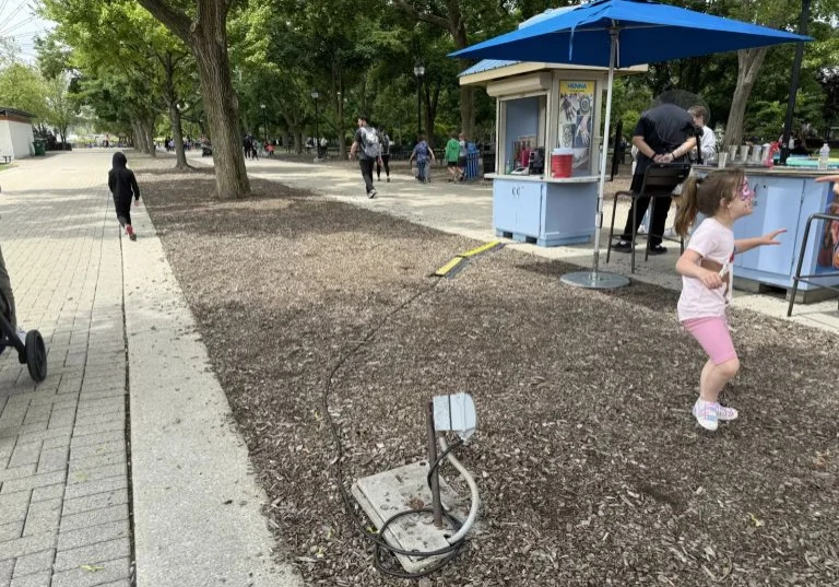 Broken outdoor electrical box with exposed conduit and extension cords running across the ground near event vendor booths.
