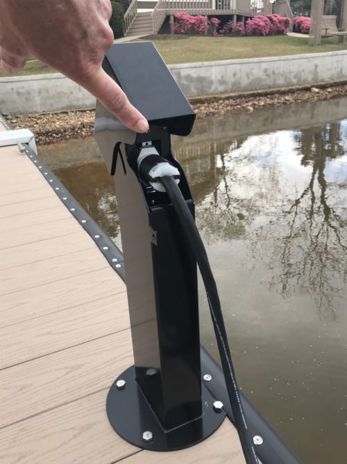 open hinged black outdoor electrical power pedestal on a dock with a charging cable connected